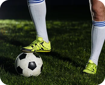 Close-up of a soccer player’s legs with cleats controlling a football on green grass during a match or training session.